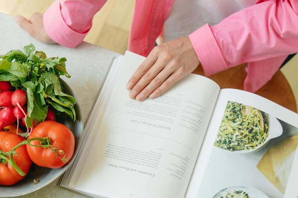 Eine Person steht vor einem Kuechentresen und liest ein Kochbuch.