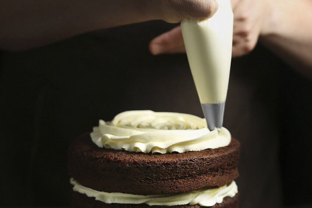 Eine Person spritzt mit einem Spritzbeutel Sahne auf einen Kuchen.