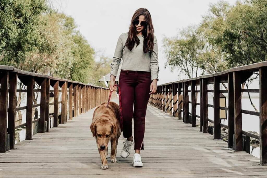 Eine Frau mit Sonnenbrille laeuft mit einem Hund ueber eine Bruecke.