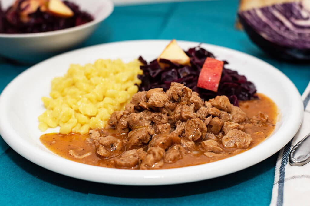 Ein veganes Ragout mit Spaetzle und Rotkraut auf einem weissen Teller.