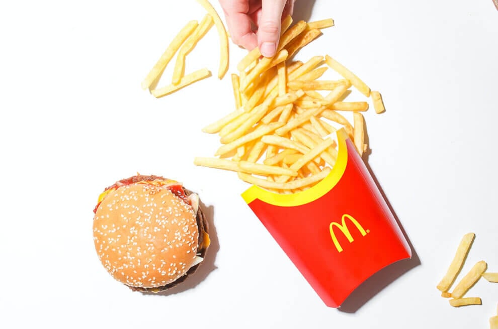 mcdonalds pommes und ein burger von oben fotografiert mit einer hand, die nach den Pommes greift