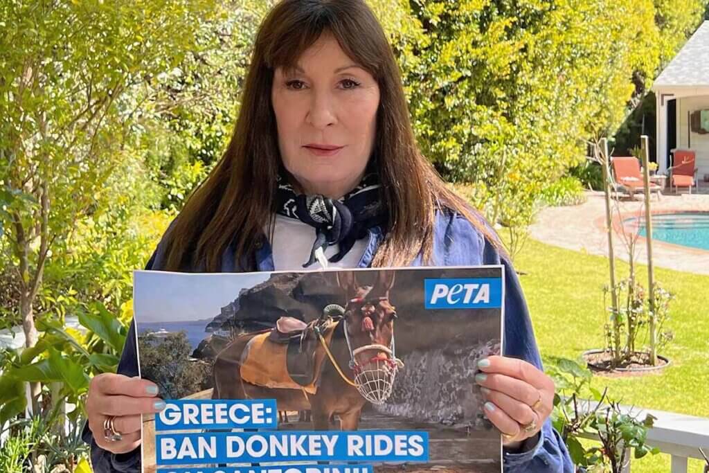 Anjelica Huston steht vor einem Garten und haelt ein Plakat in der Hand.