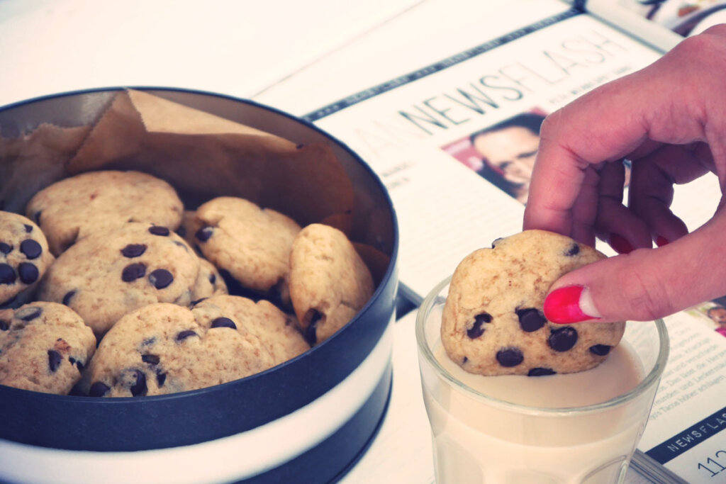 Eine Person tunkt einen Chocolate Chip Cookie in ein Glas Milch.