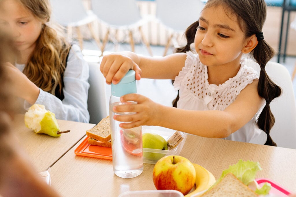 Kinder sitzen am Tisch in der Schule und essen.