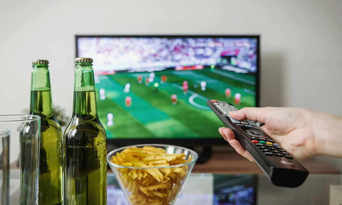 Im Fernseher läuft Fußball und auf dem Tisch steht Bier und Chips