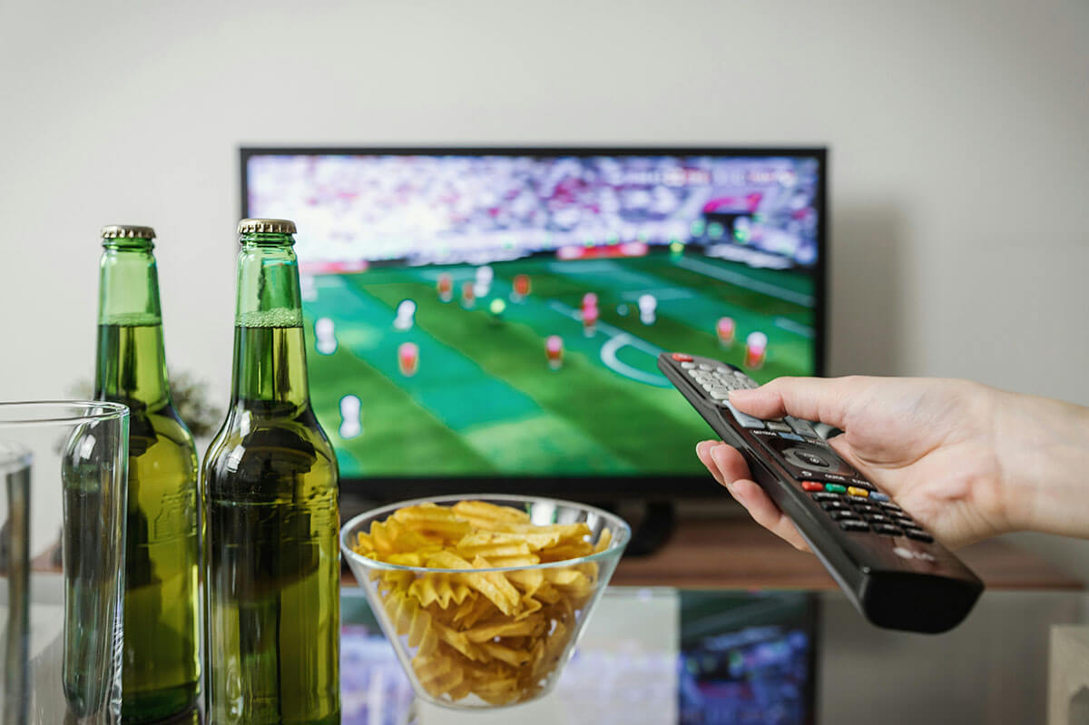 Im Fernseher läuft Fußball und auf dem Tisch steht Bier und Chips