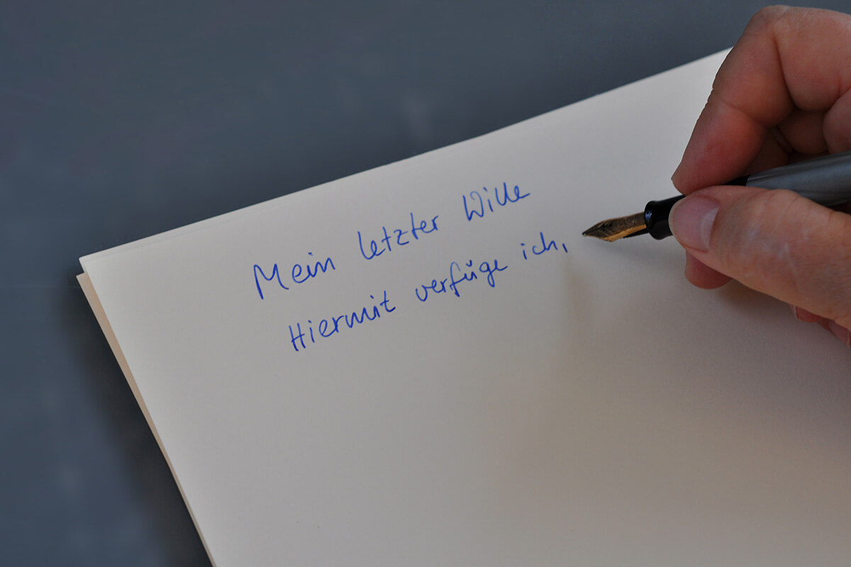 Eine Person schreibt mit einem Fueller auf ein Blatt papier ihren letzten Willen.