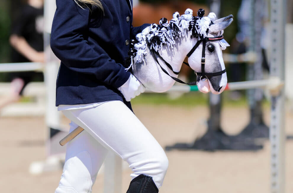 Eine Person in Reituniform reitet auf einem weissen Steckenpferd.