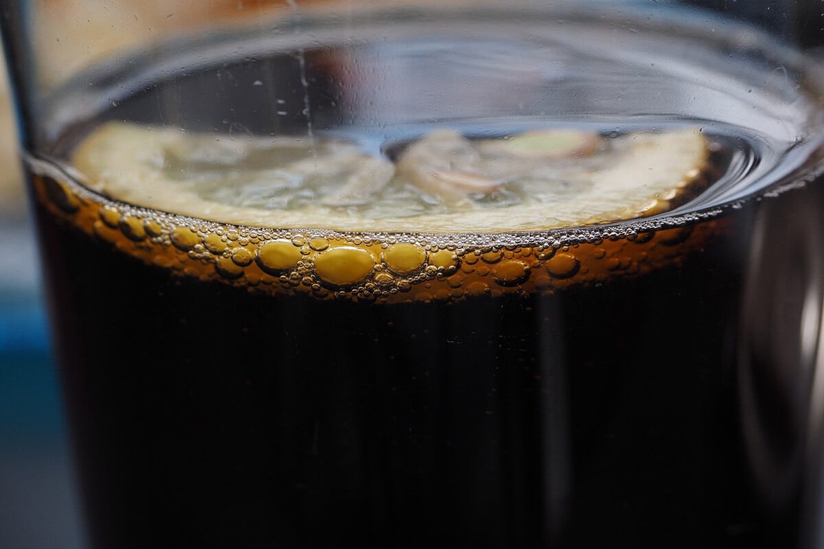 Nahaufnahme von einem Glas mit Cola und einer halben Zitronenscheibe.