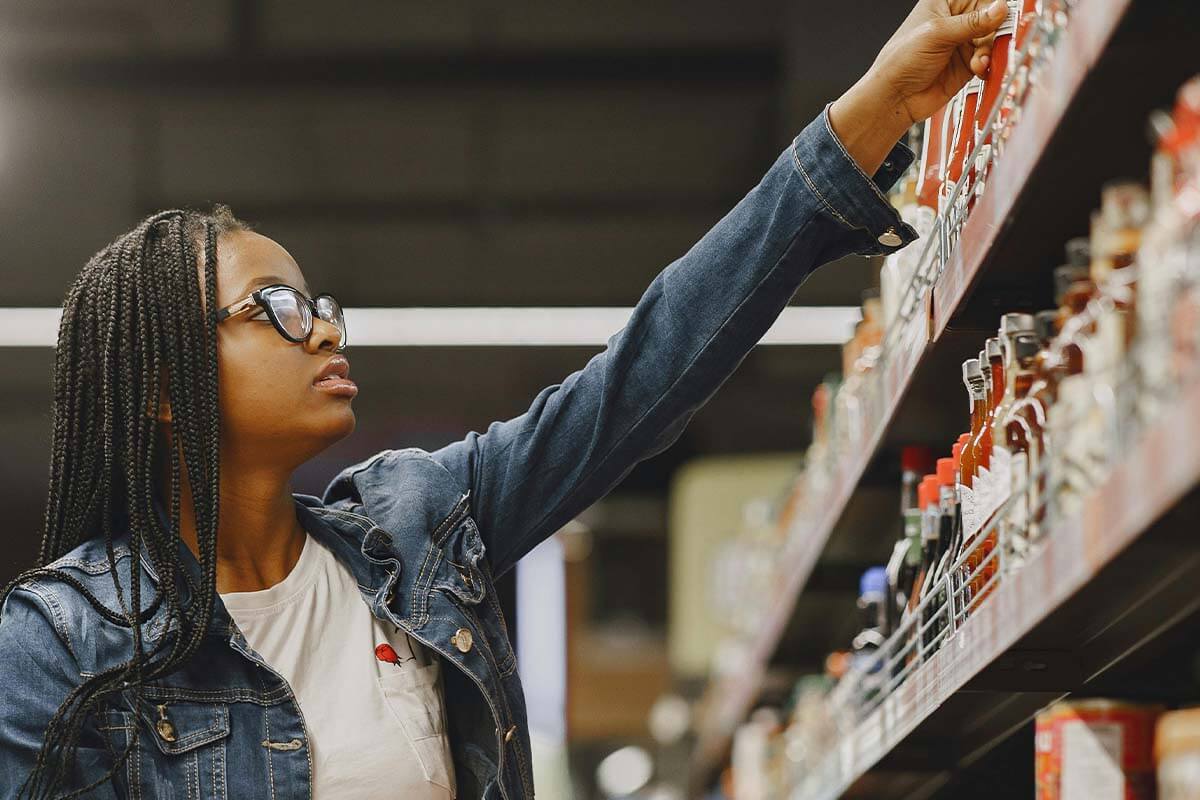 Eine Frau greift im Supermarkt nach einem Produkt im Regal.