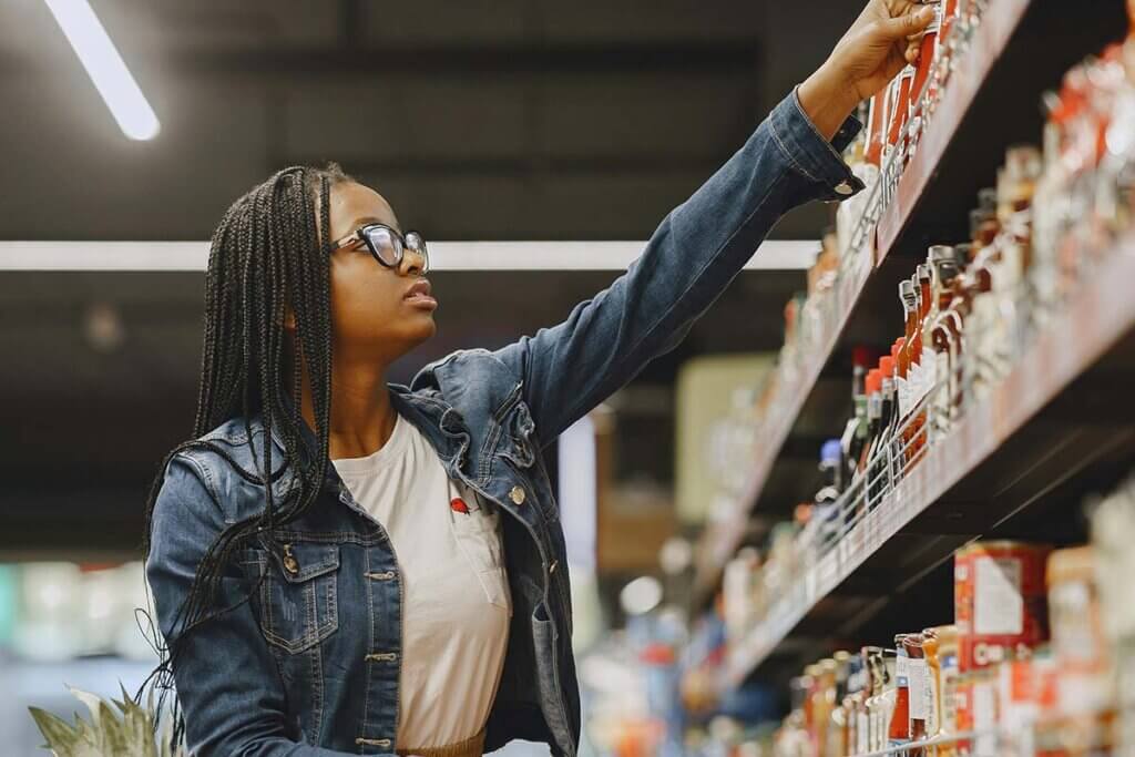 Eine Frau steht vor einem Supermarktregal und greift nach einem Produkt.