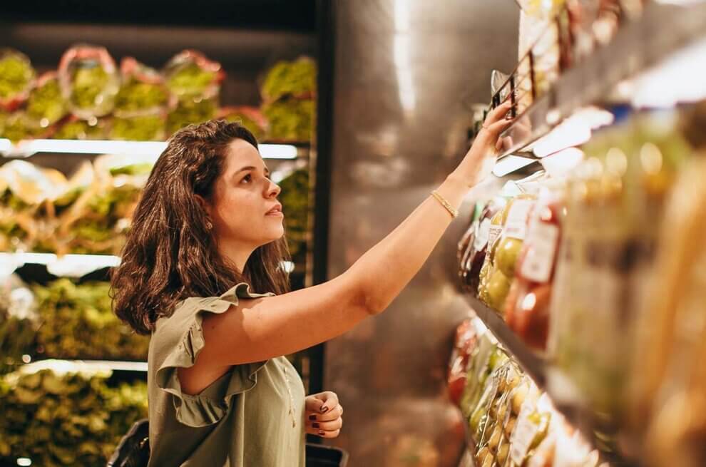 Eine Frau steht vor einem Supermarktregal und schaut nach Produkten.