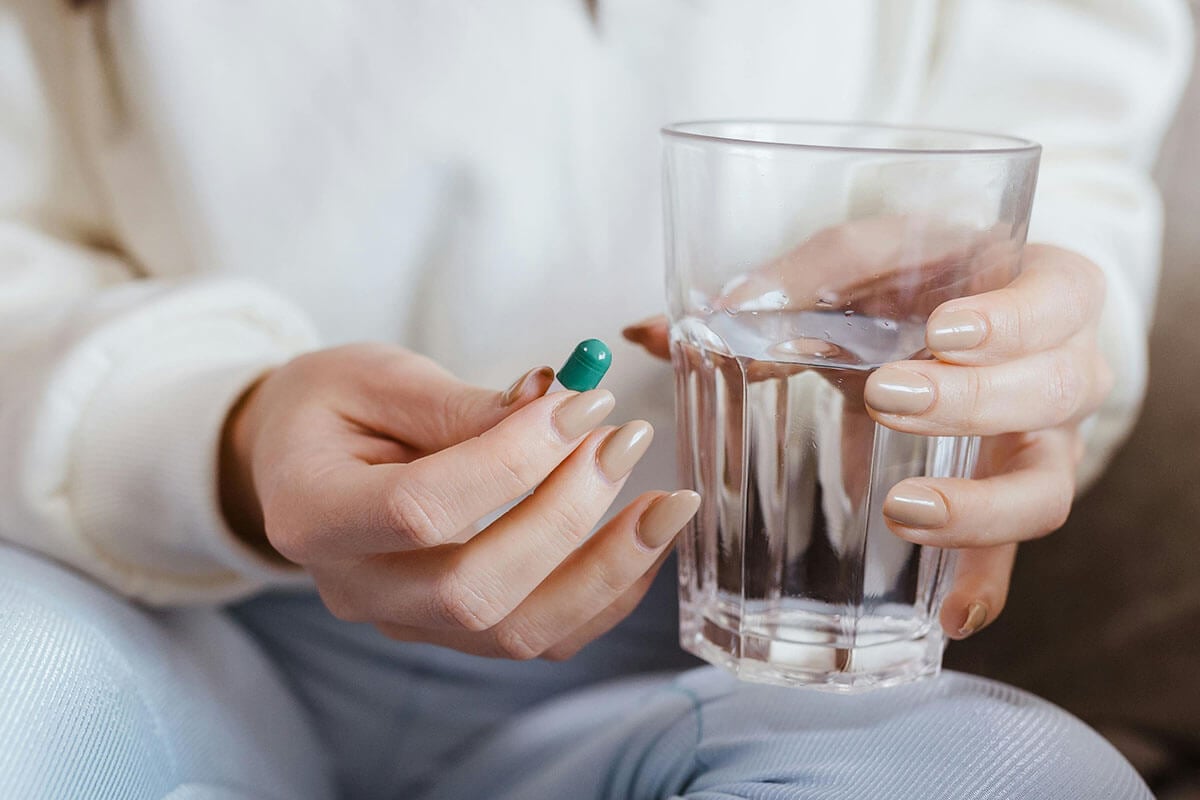 Frau hat ein Glas mit Wasser und eine Kapsel in der Hand.